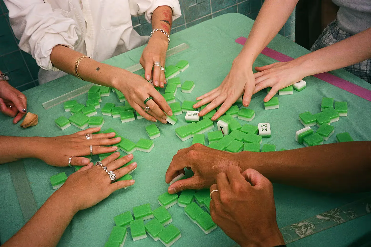 Players shuffling green-backed Mahjong tiles together around a table