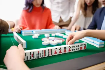 Players arranging Chinese Mahjong hands together around a green table