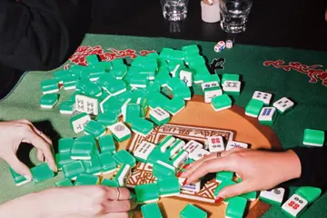 Players mixing green-backed Mahjong tiles on a patterned mat