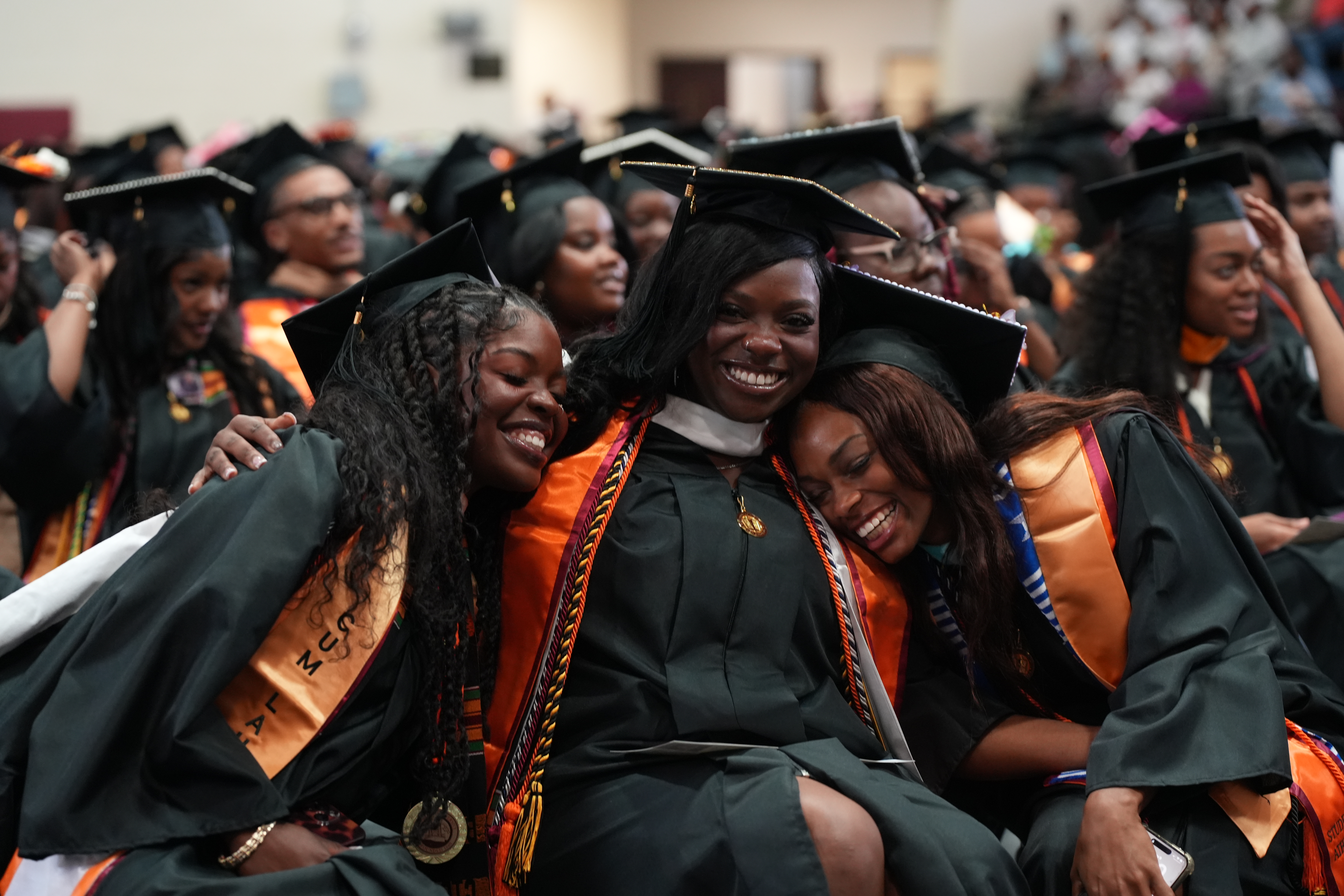 Three Claflin graduates in caps and gowns embracing at commencement