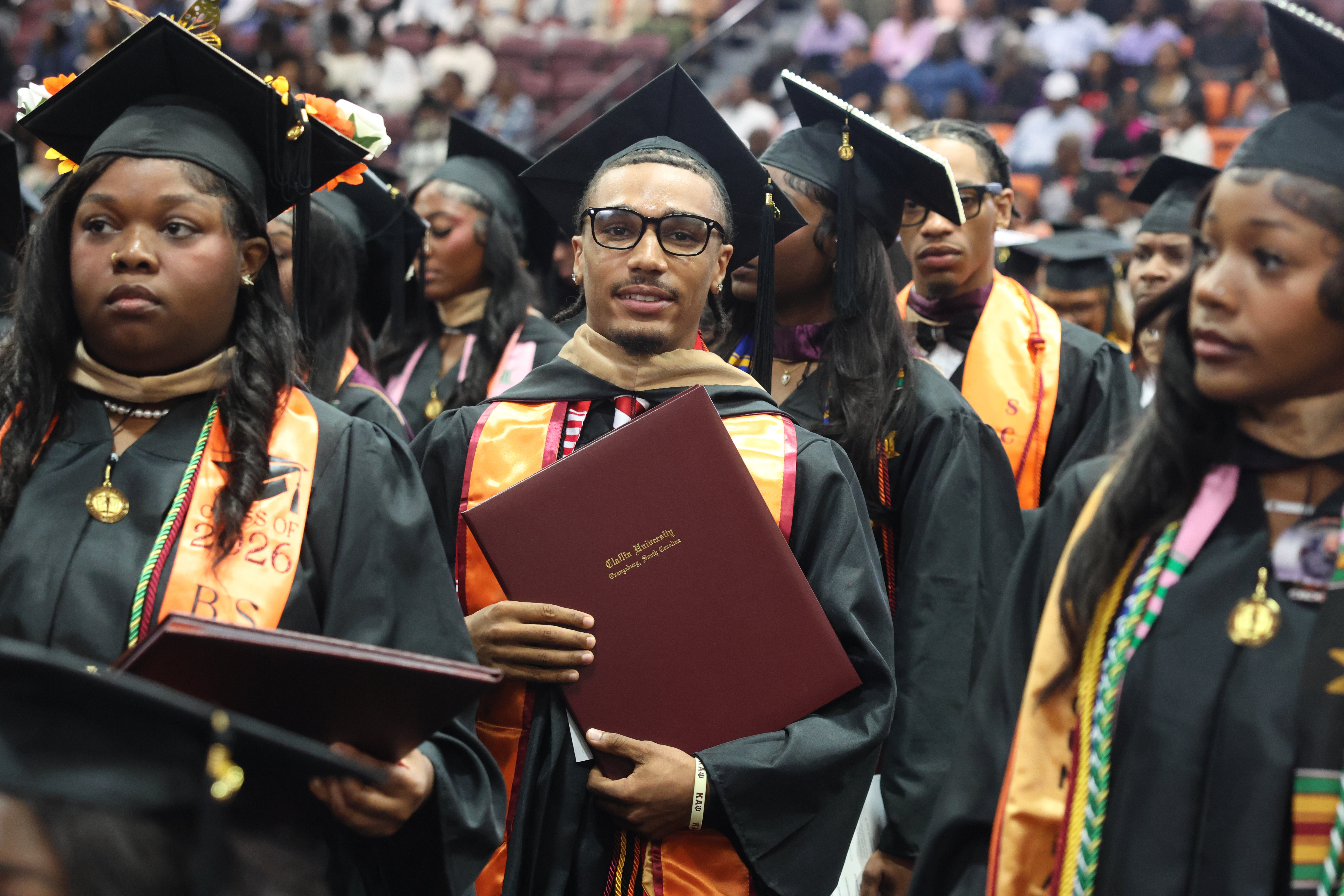Claflin graduates in caps, gowns, and orange stoles holding their diplomas