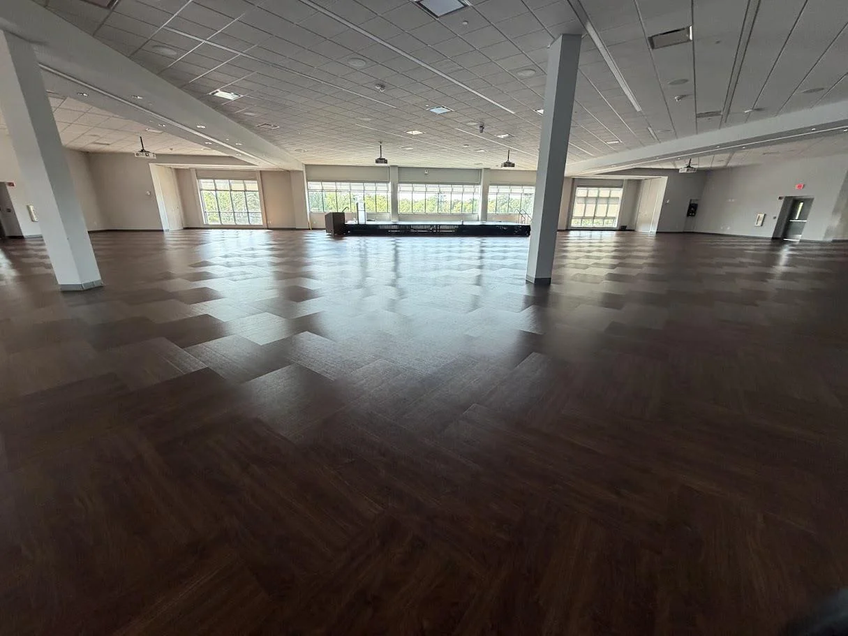 Wide view of the ballroom with dark wood floors, white columns, and large windows