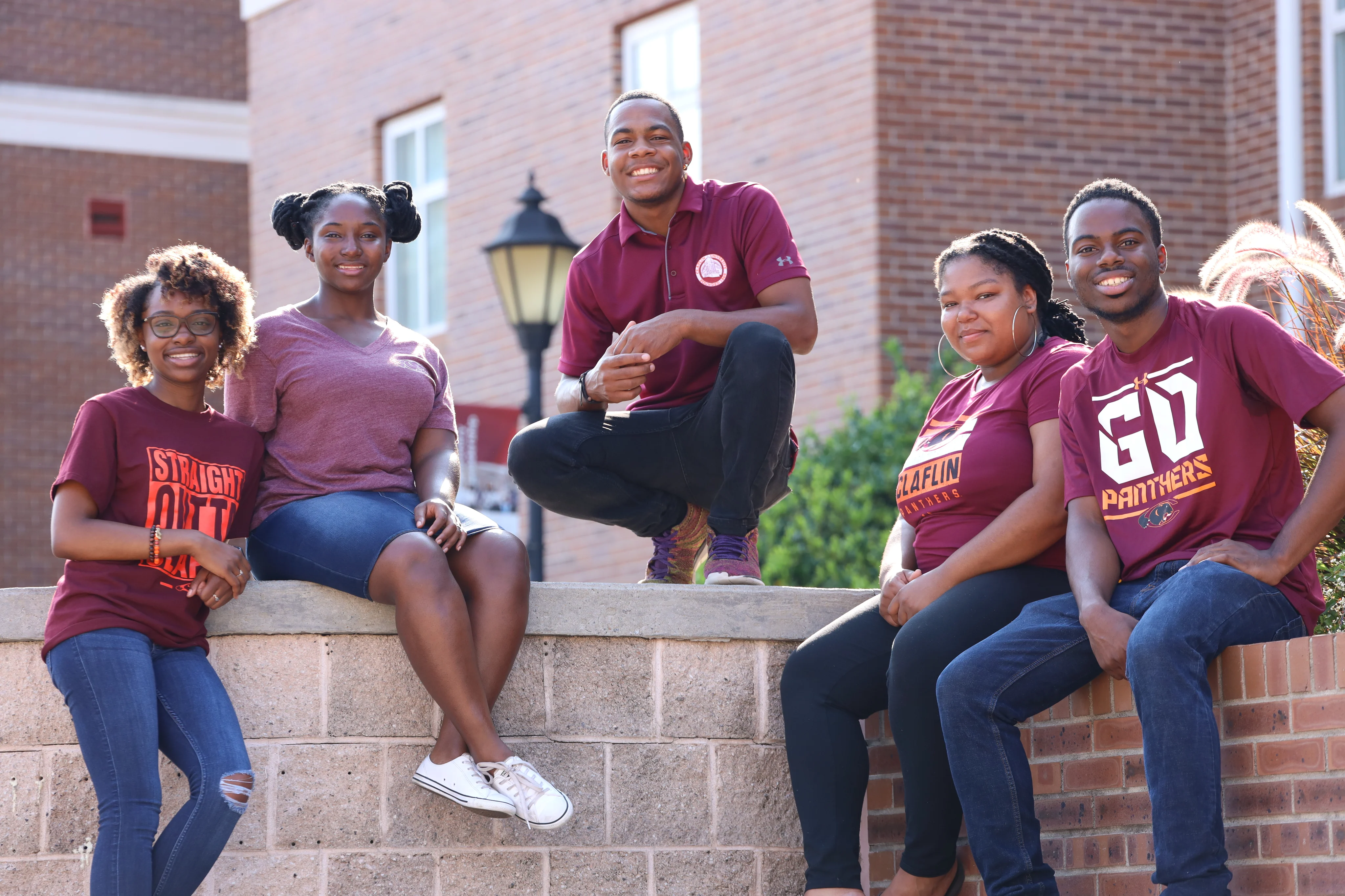 Five smiling Claflin students in maroon Panthers shirts gathered in a campus courtyard
