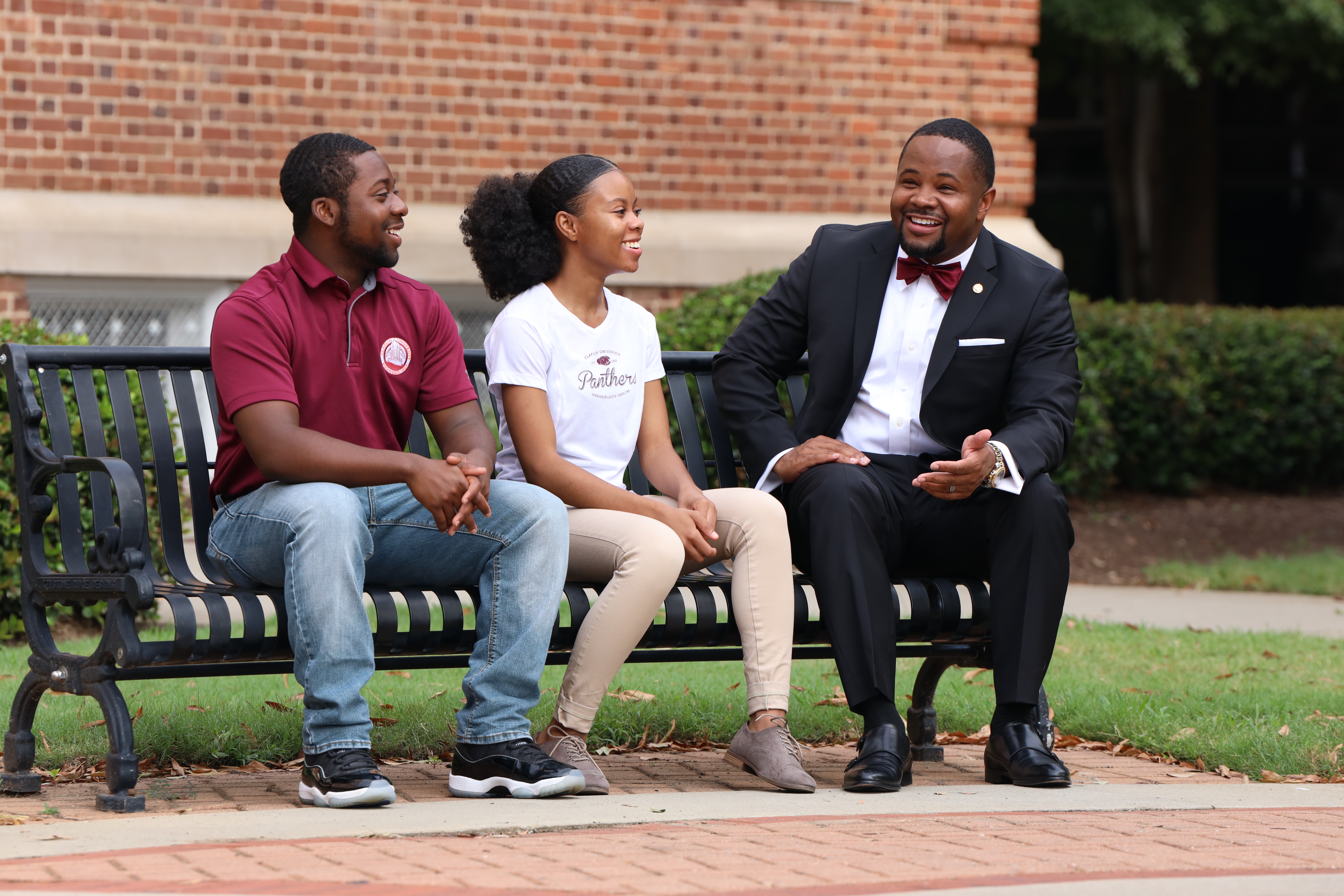 Two Claflin students in conversation with a university leader on a campus bench