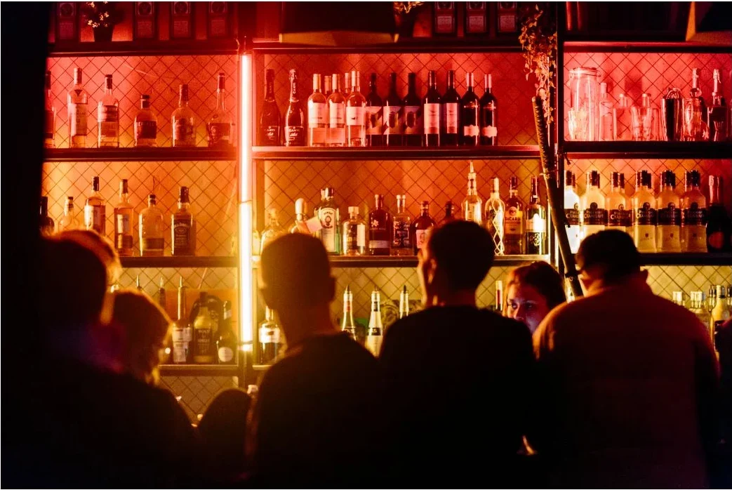 A busy bar with guests gathered beneath warm red light