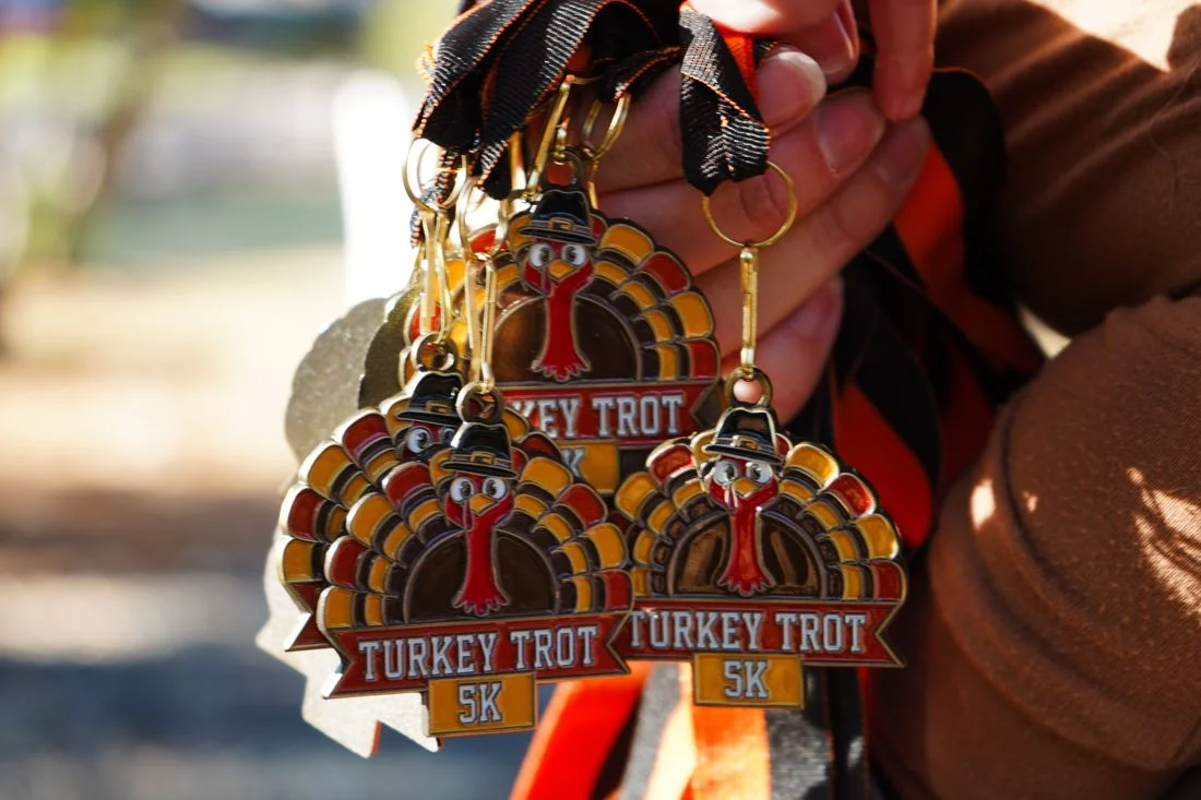 Three turkey-shaped Turkey Trot 5K finisher medals held up together.