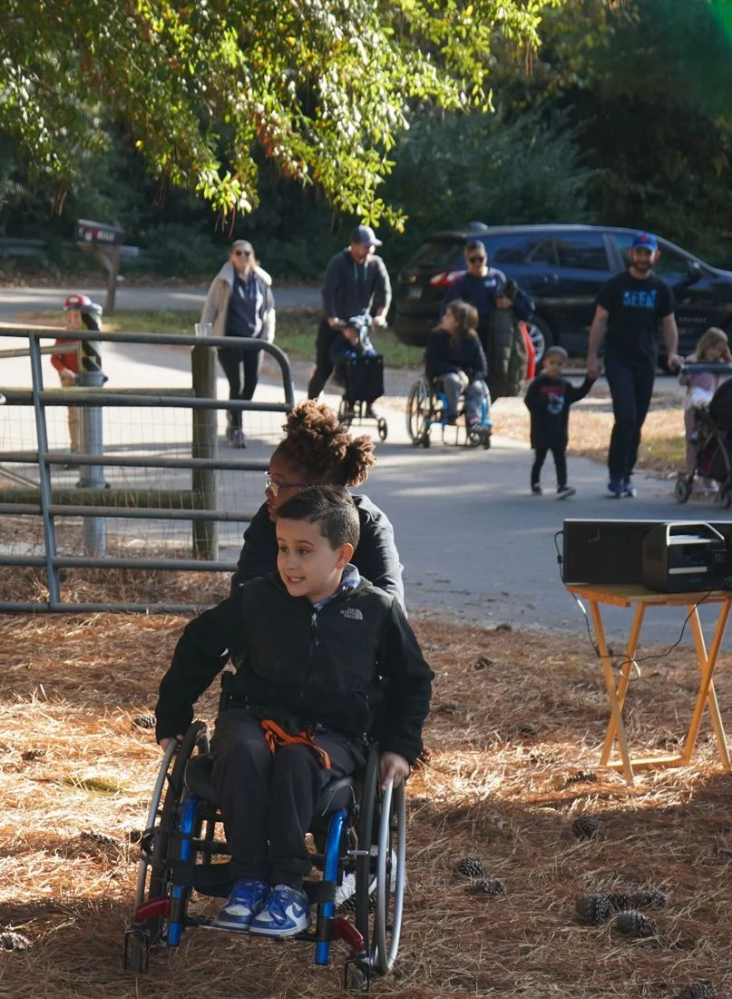 A child in a wheelchair heads down the path, with other participants walking behind.