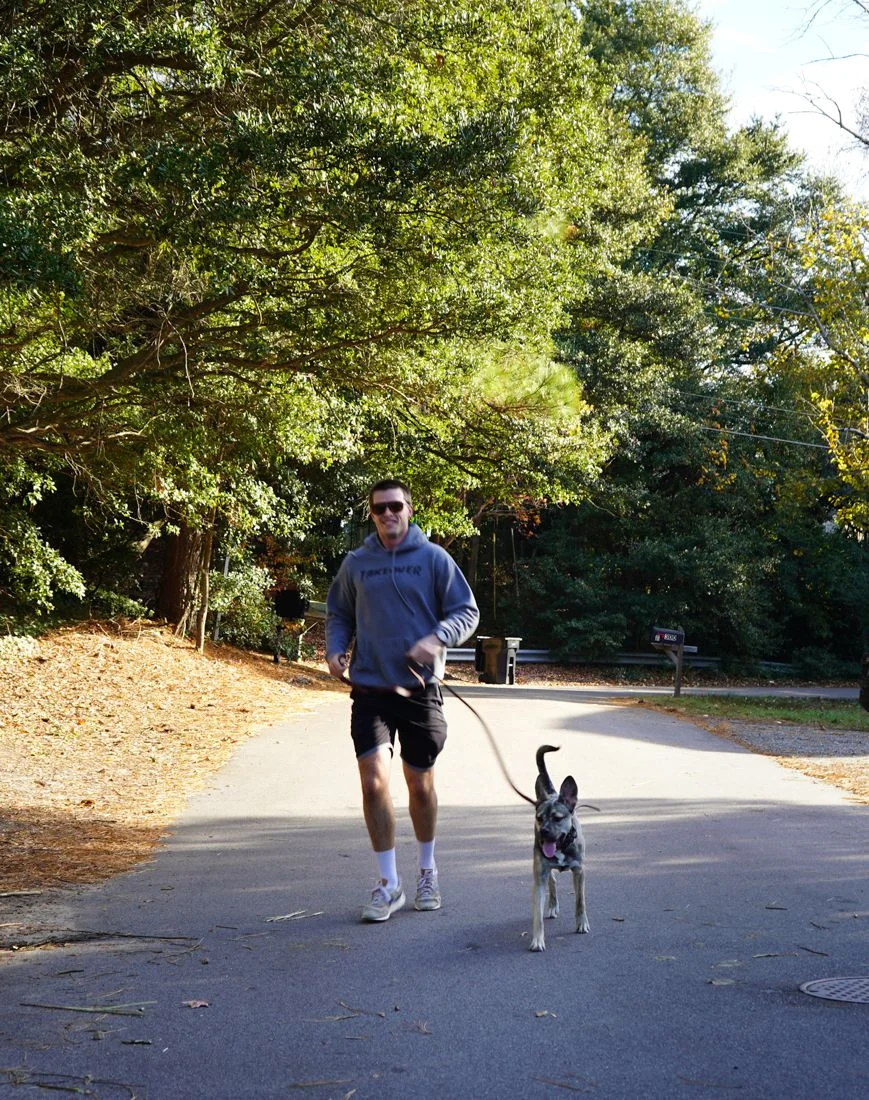 A man walks a dog on a leash down the paved path.