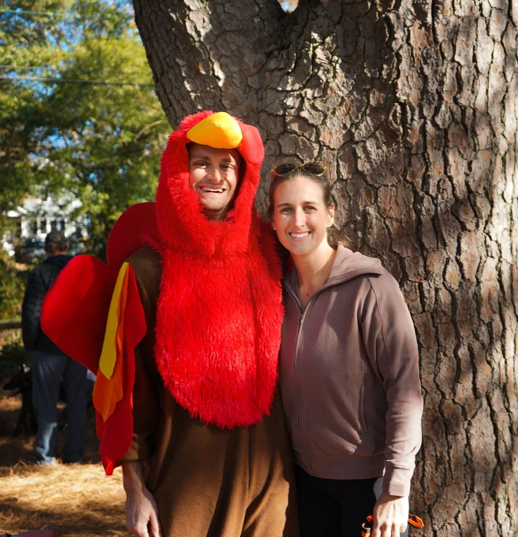 A man in a red turkey costume poses with a woman beside a tree.