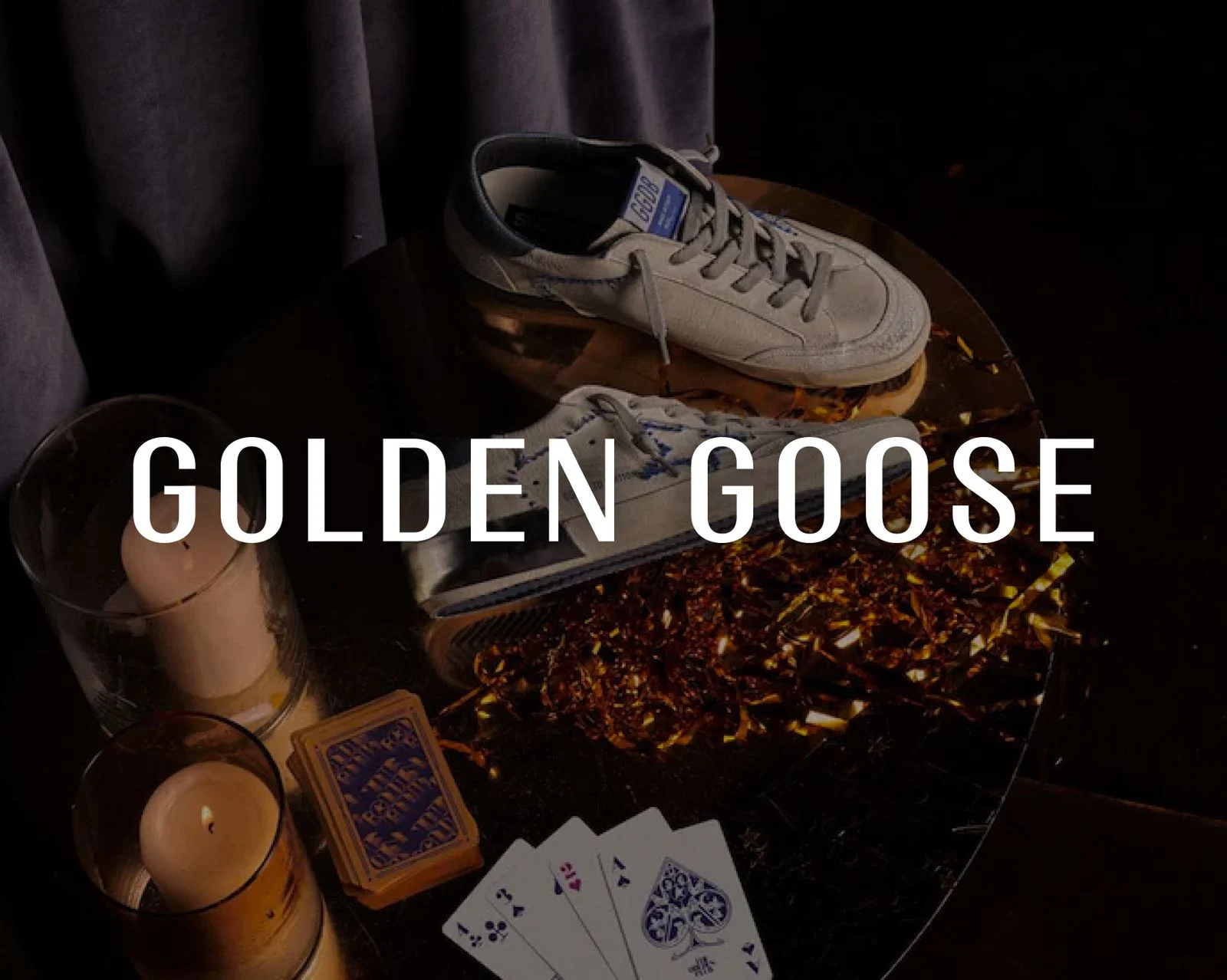 Golden Goose sneakers on a table with candles and playing cards, with the Golden Goose wordmark