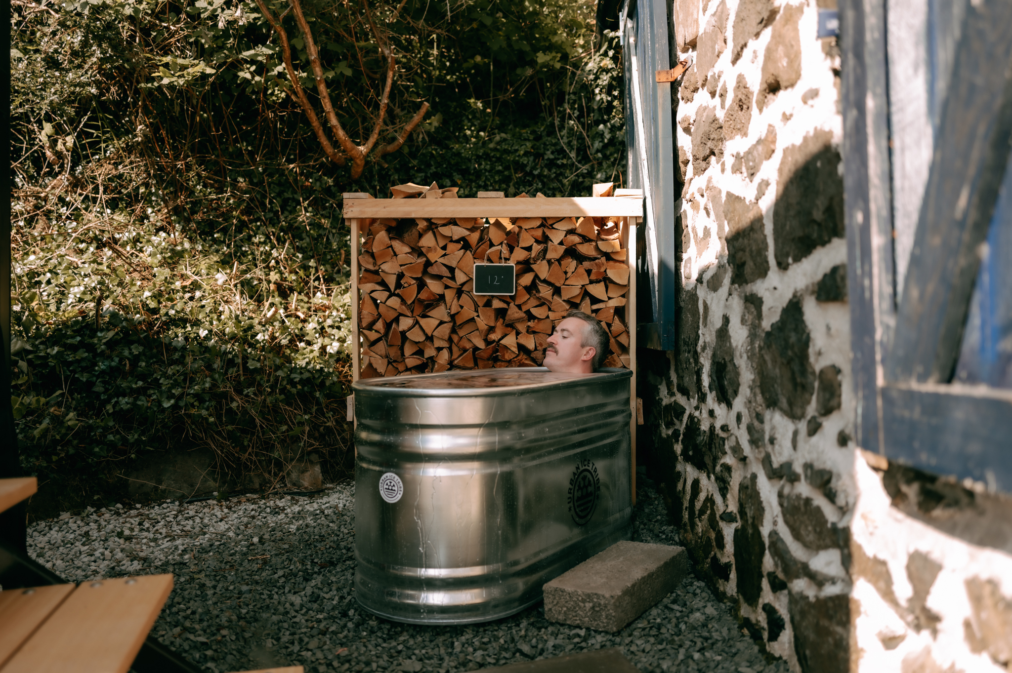 A guest relaxing in the cold plunge beside the firewood stack