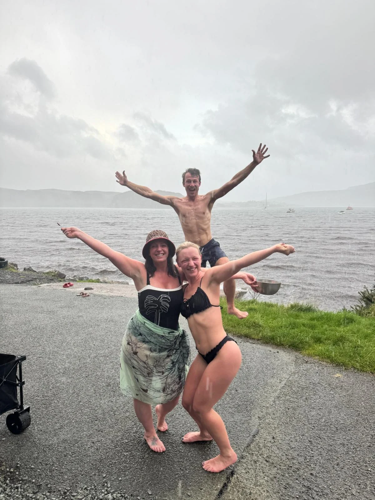Three sauna guests smiling beside the water in Portree