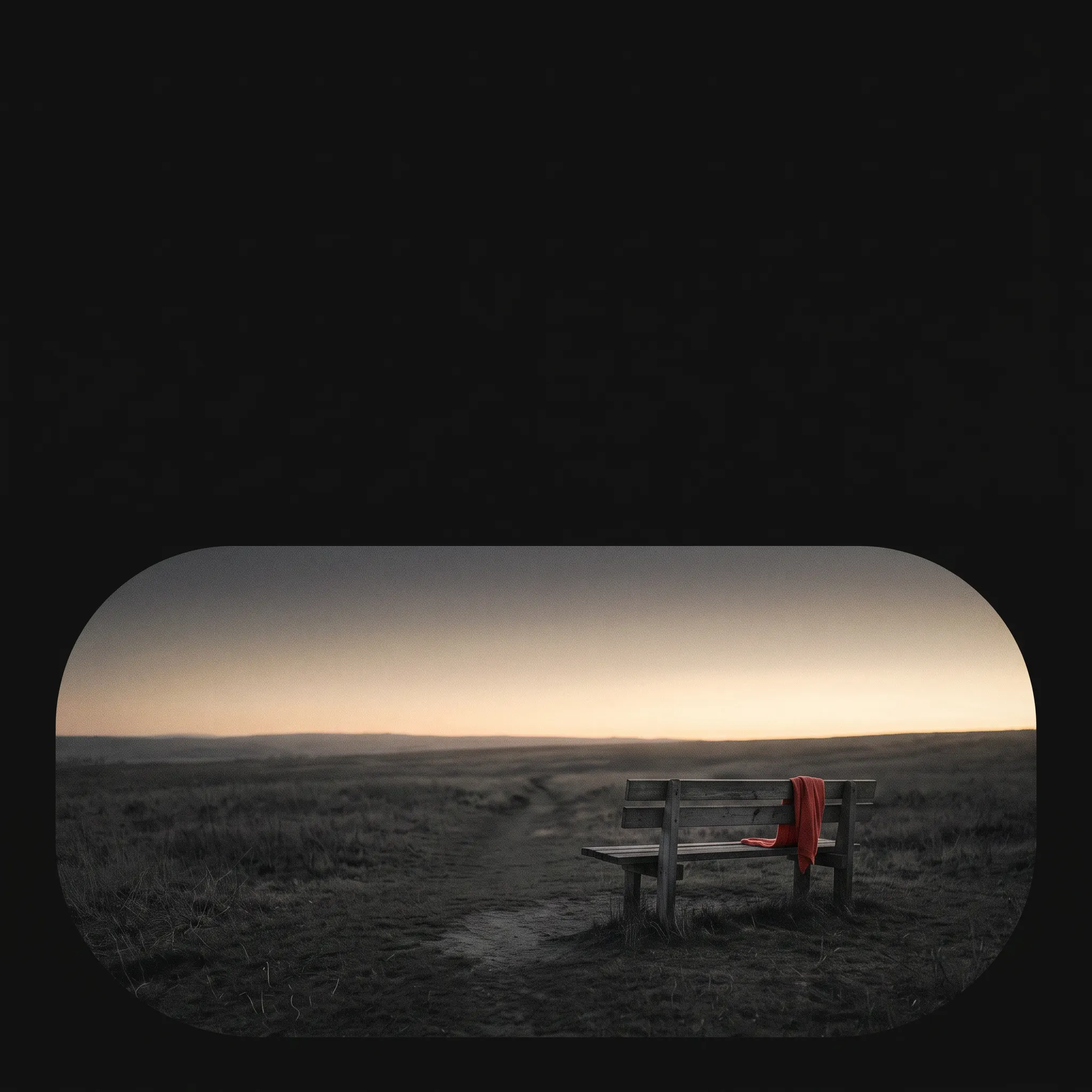An empty bench at dusk framed inside one wide capsule landscape