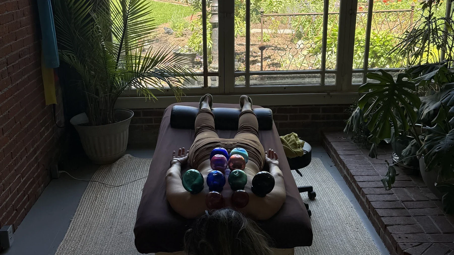 A patient resting on the treatment table with glass cups, facing the garden window and plants