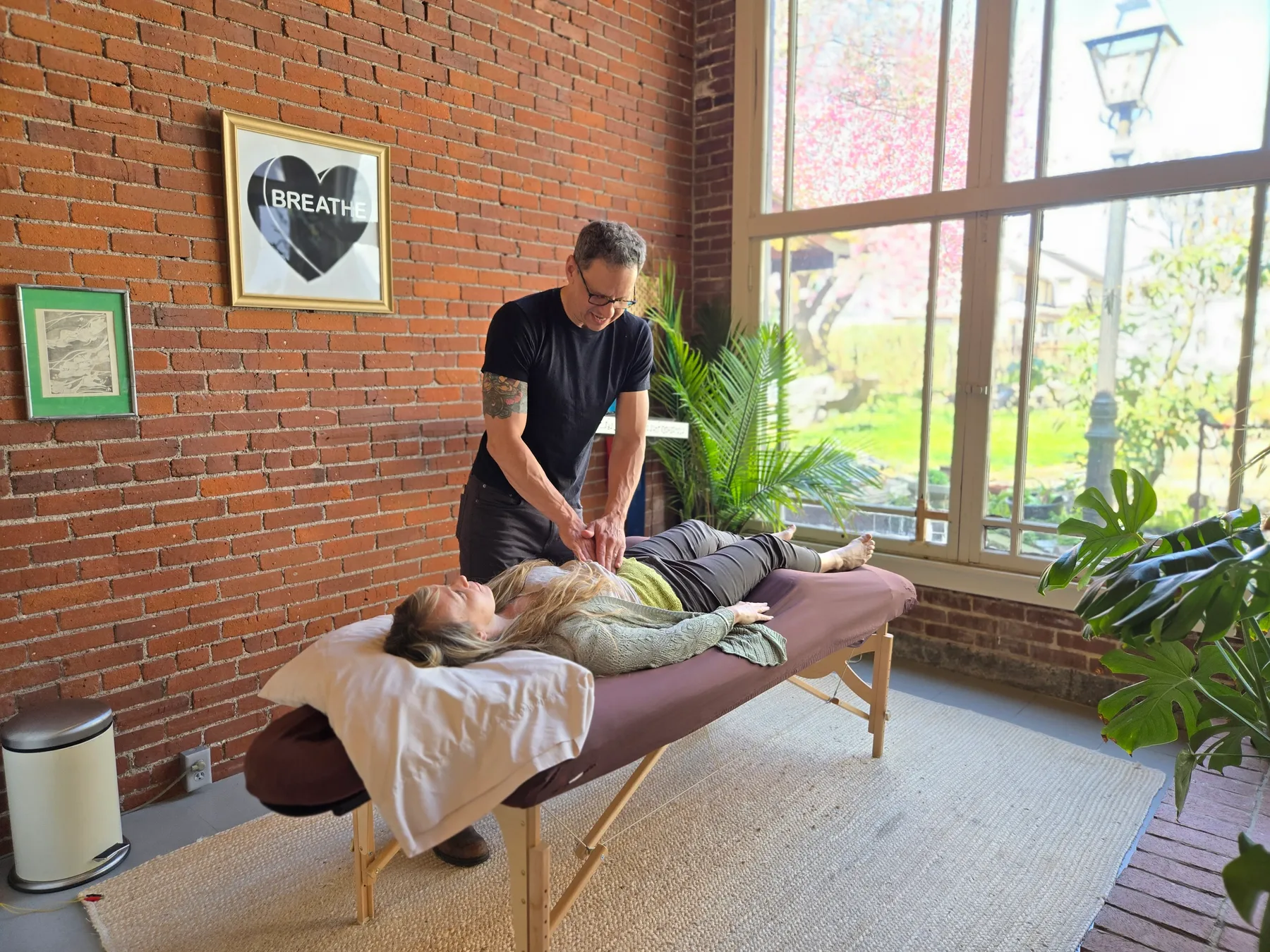 Jason Rinker treating a patient lying face-up by the big garden window
