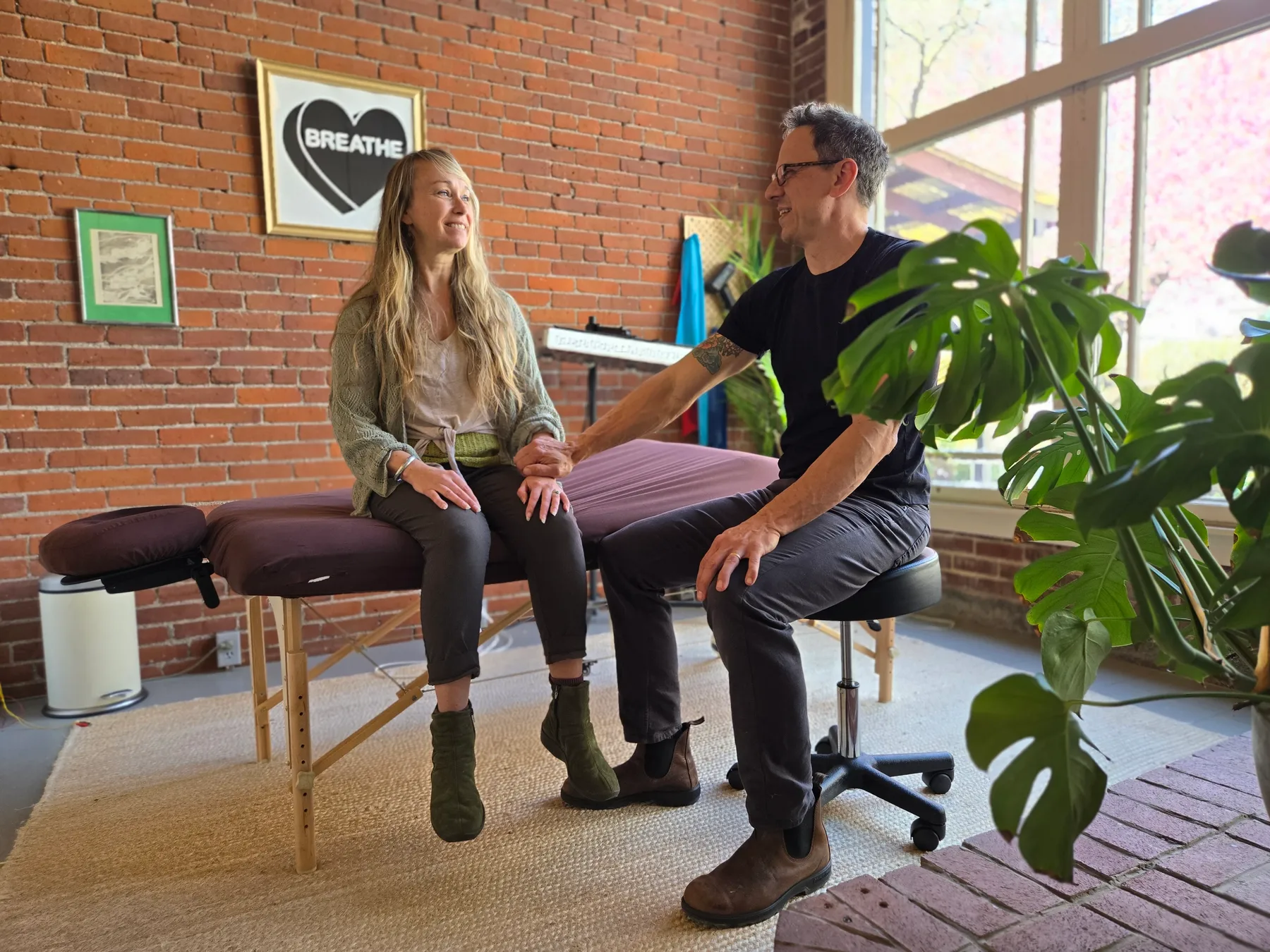 Jason Rinker and a patient talking and smiling in his brick-walled treatment room