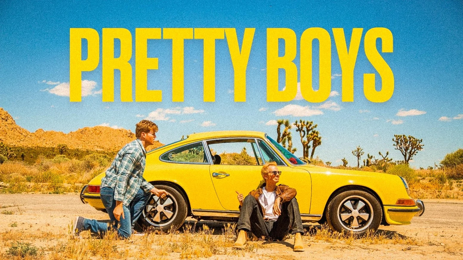 Pretty Boys campaign art with a yellow car and its two leads on a sunny desert road