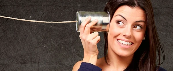 Mujer escuchando a través de un teléfono hecho con una lata y un cordel