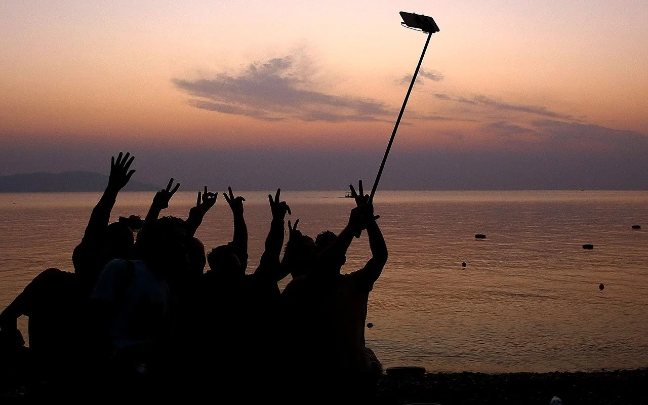 Grupo de adolescentes fotografiándose con un palo para selfis al atardecer