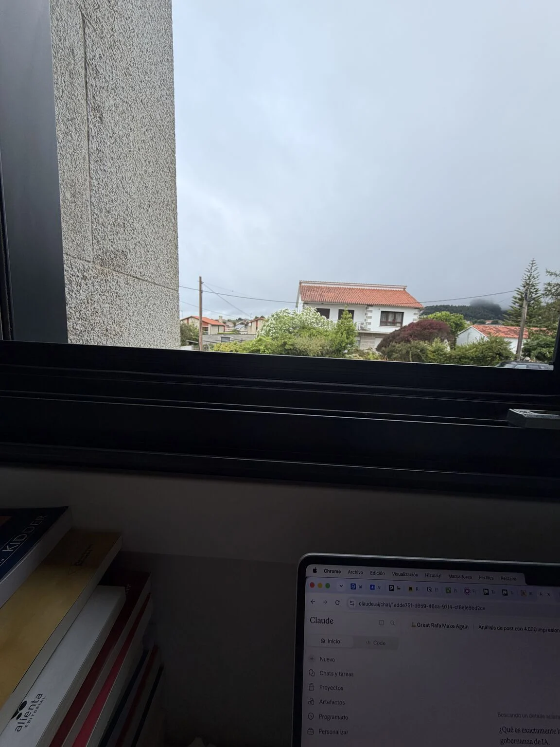 Portátil abierto junto a una ventana con vistas a un día nublado en Sangenjo
