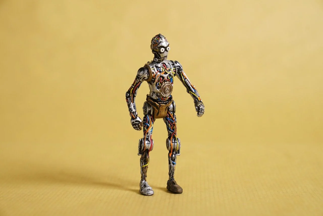Figura de un robot construida con piezas y cables sobre un fondo amarillo