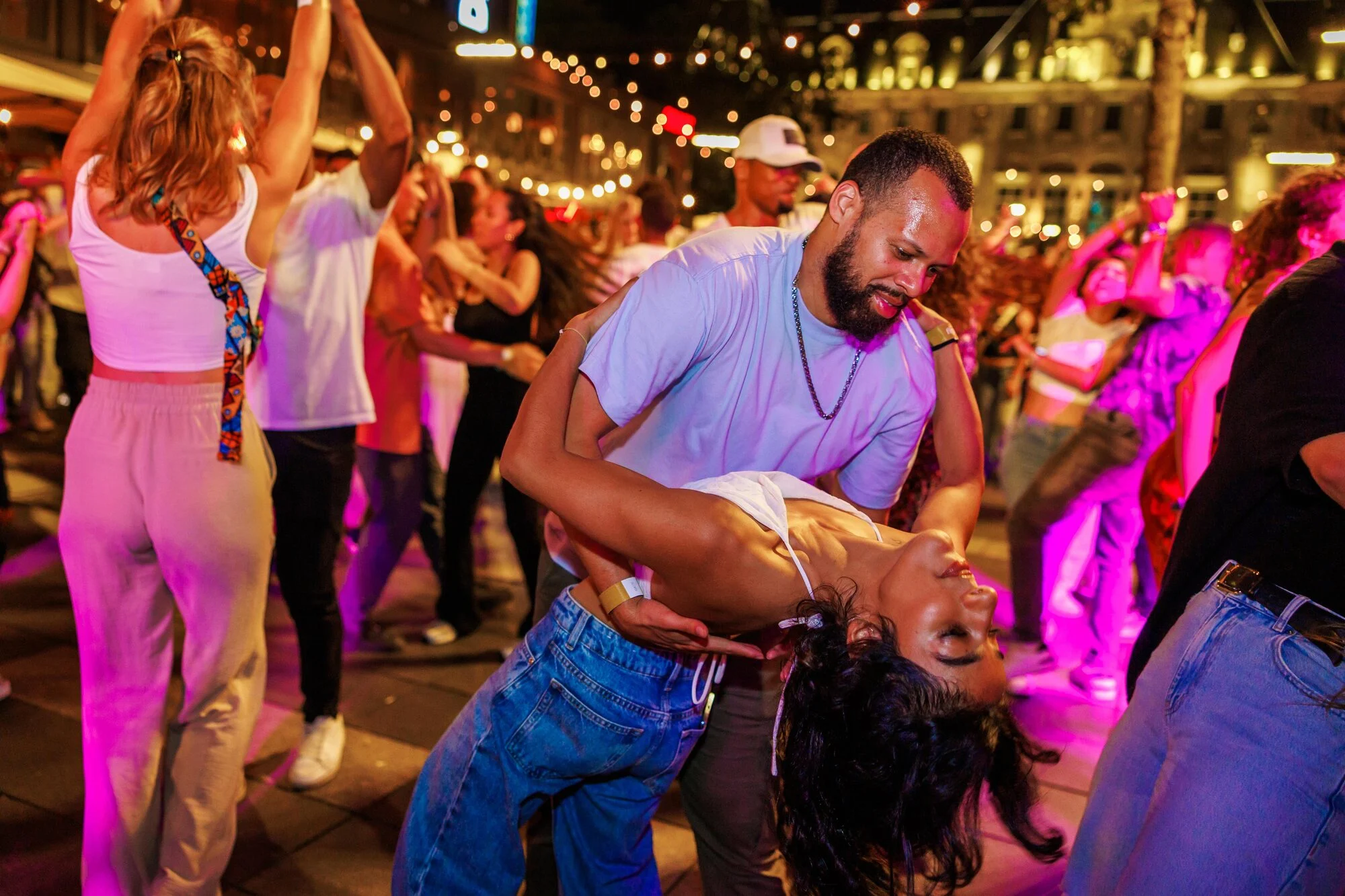 A dancer dips his partner on a crowded, string-lit Latin dance floor