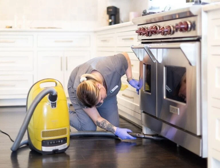 Vella’s staff cleaning the bottom of a stove using a Miele vacuum cleaner.