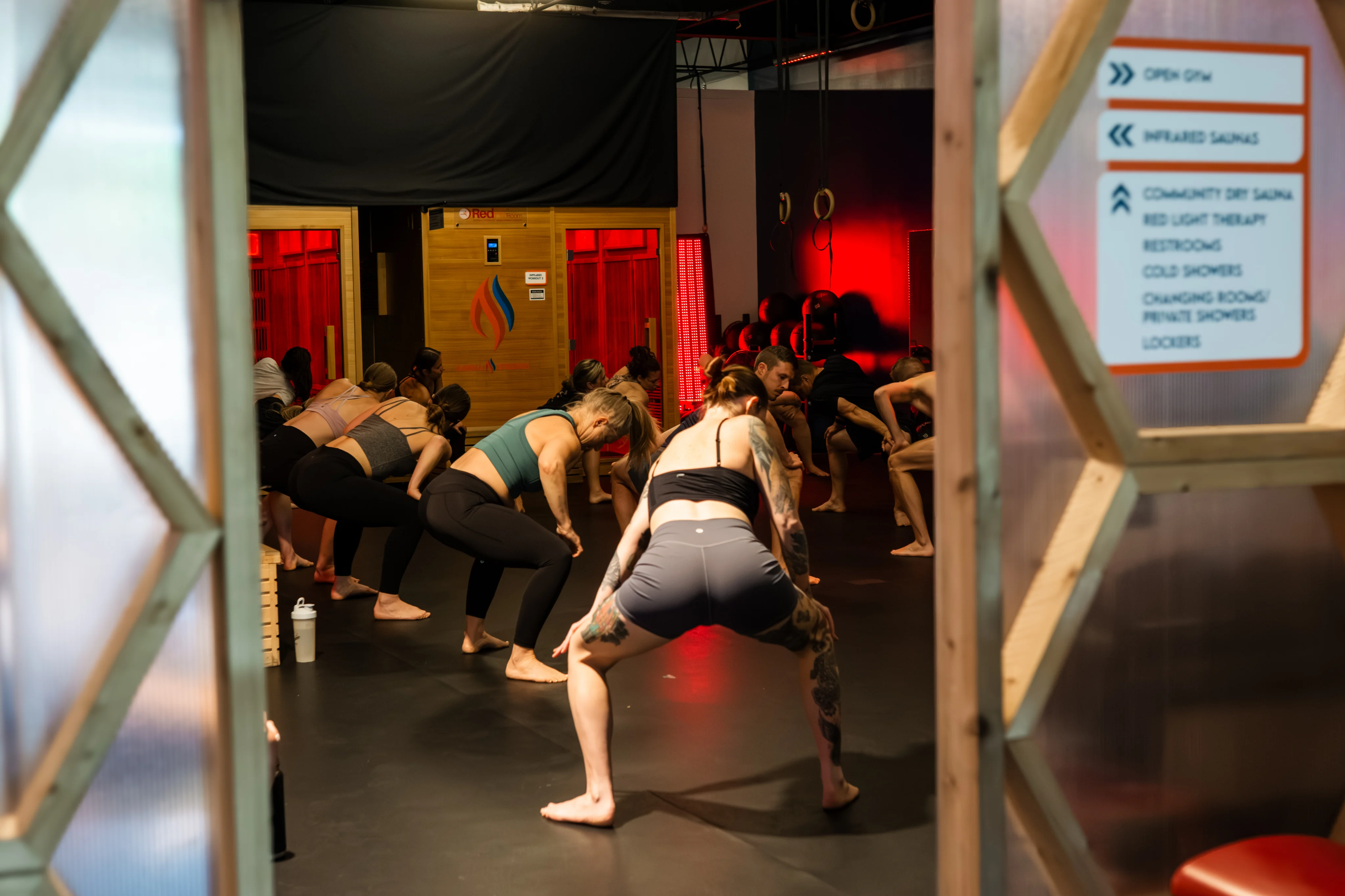 Sauna Strong members performing squats together during a group workout under red lighting